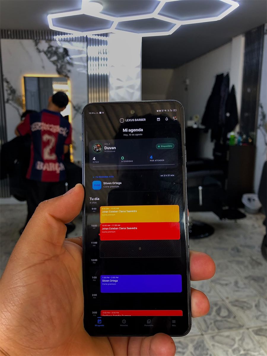 Celular dentro de la barbería Lexus Barber mostrando la agenda del día de un profesional en la app de Dornex, con el local al fondo